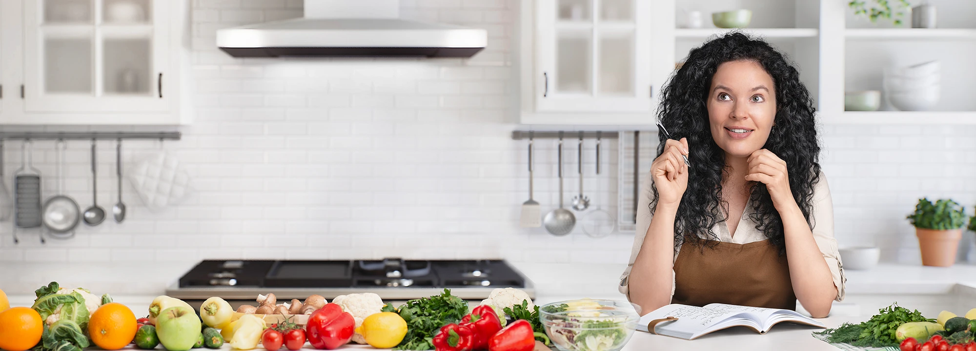 Yana in a bright kitchen surrounded by fresh vegetables while planning recipes for Delica Recipes.
