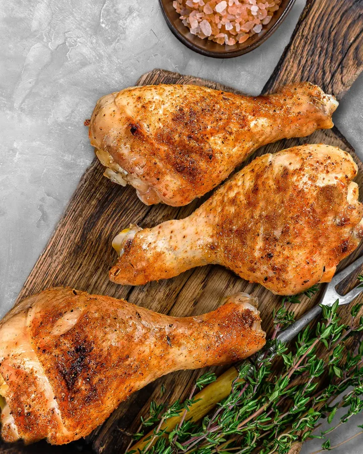 Baked chicken drumsticks on a wooden serving board coated with smoked paprika and herbs, highlighting their freshly roasted skin.