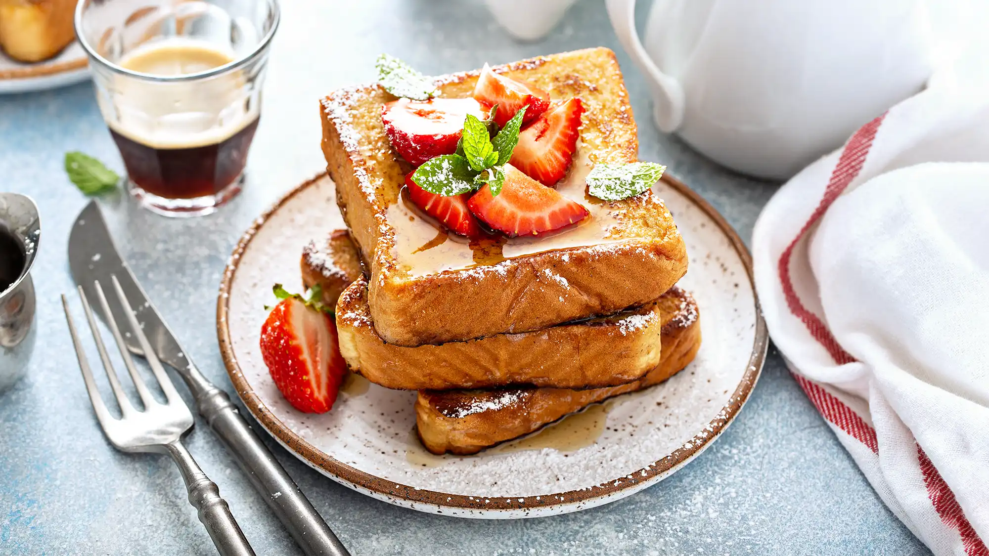 A cozy breakfast scene featuring French Toast topped with fresh strawberries and served alongside a cup of coffee.