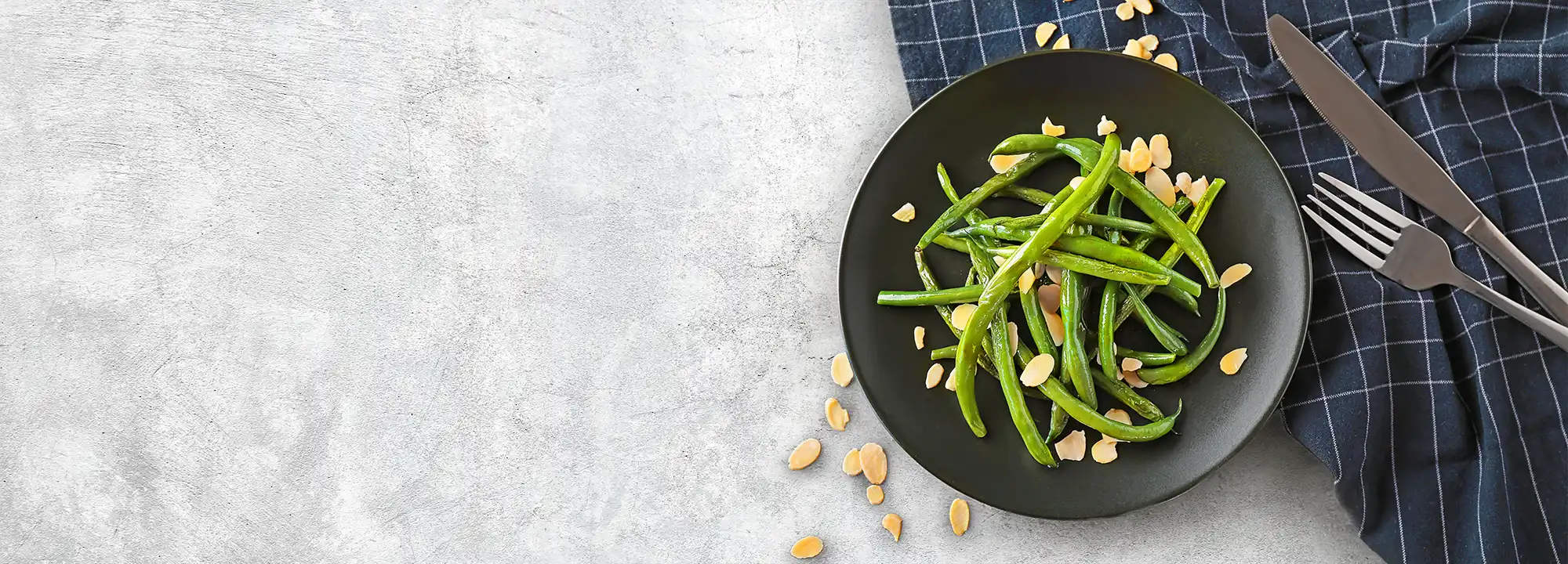 Green Beans Almondine sprinkled with toasted almonds, placed beside cutlery and a napkin, showing how the dish is served at the table.