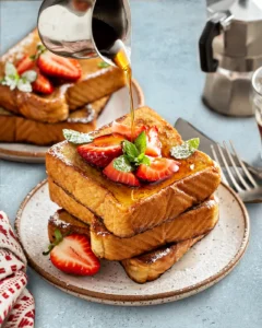 Maple syrup pouring over a tall stack of golden French Toast.