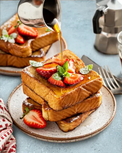 Maple syrup pouring over a tall stack of golden French Toast.