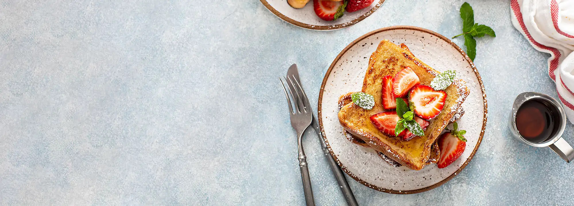 Overhead view of French Toast drizzled with maple syrup and topped with strawberries, ready to serve for breakfast or brunch.