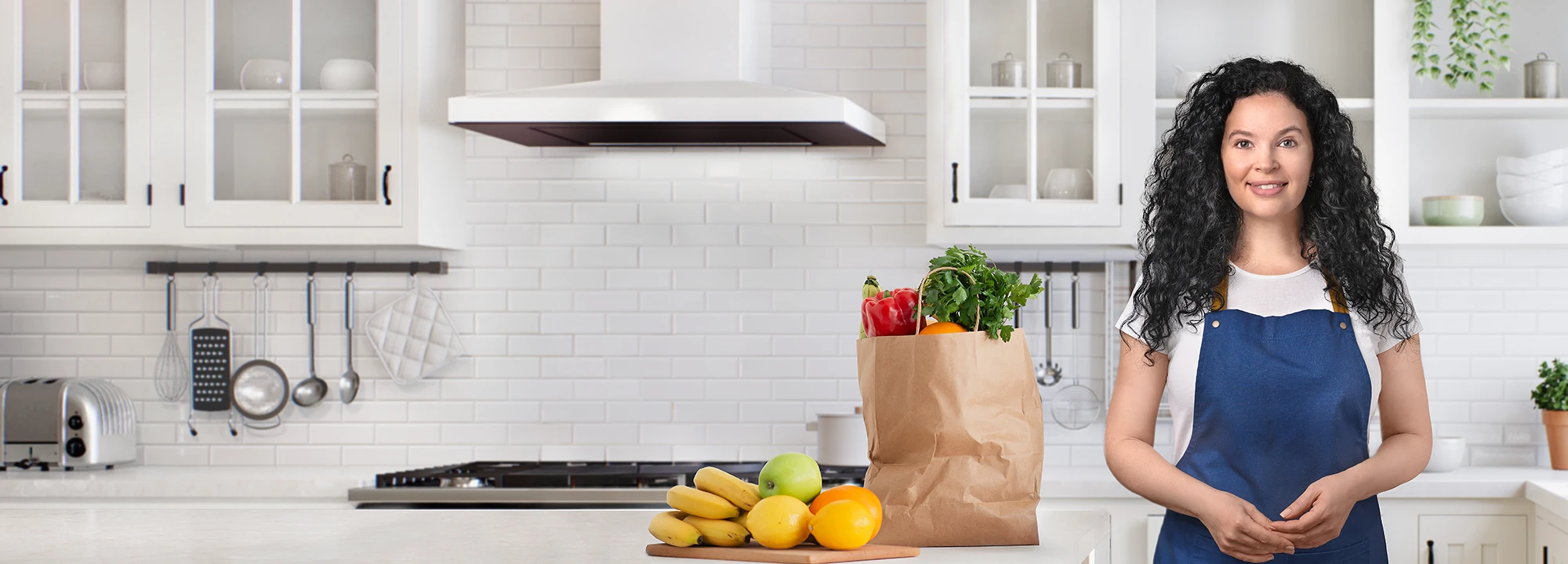 Yana smiling in her kitchen beside a grocery bag filled with fresh produce, inviting visitors to connect with Delica Recipes.